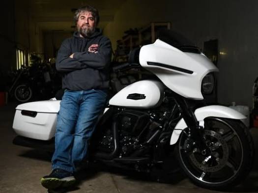 modern motorcycle repair, concentrated expression, tightening bolts, photorealistic, open workshop with wooden workbenches and hanging tools, highly detailed, dust particles in the air, 50mm lens, cool colors, natural morning lighting